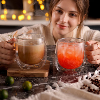 A woman holding two double-wall mugs with coffee and a pink iced drink.